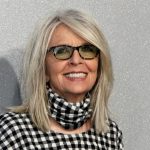 Diane Keaton smiling on a red carpet in a classic outfit