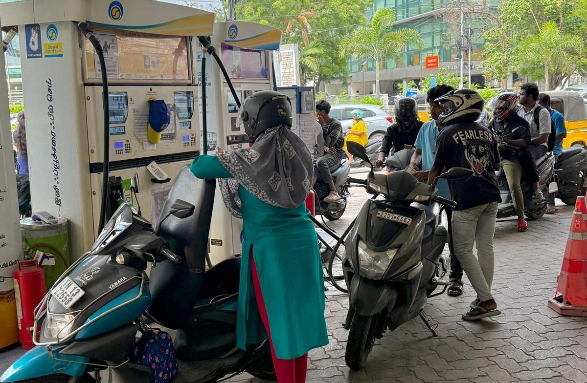 A person refilling a vehicle at a petrol pump in New Delhi showing the India fuel price hike on the digital meter.