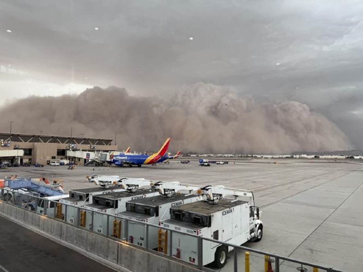 A massive, towering wall of brown dust swallowing high-rise buildings and highways in Phoenix Arizona during a severe monsoon storm.